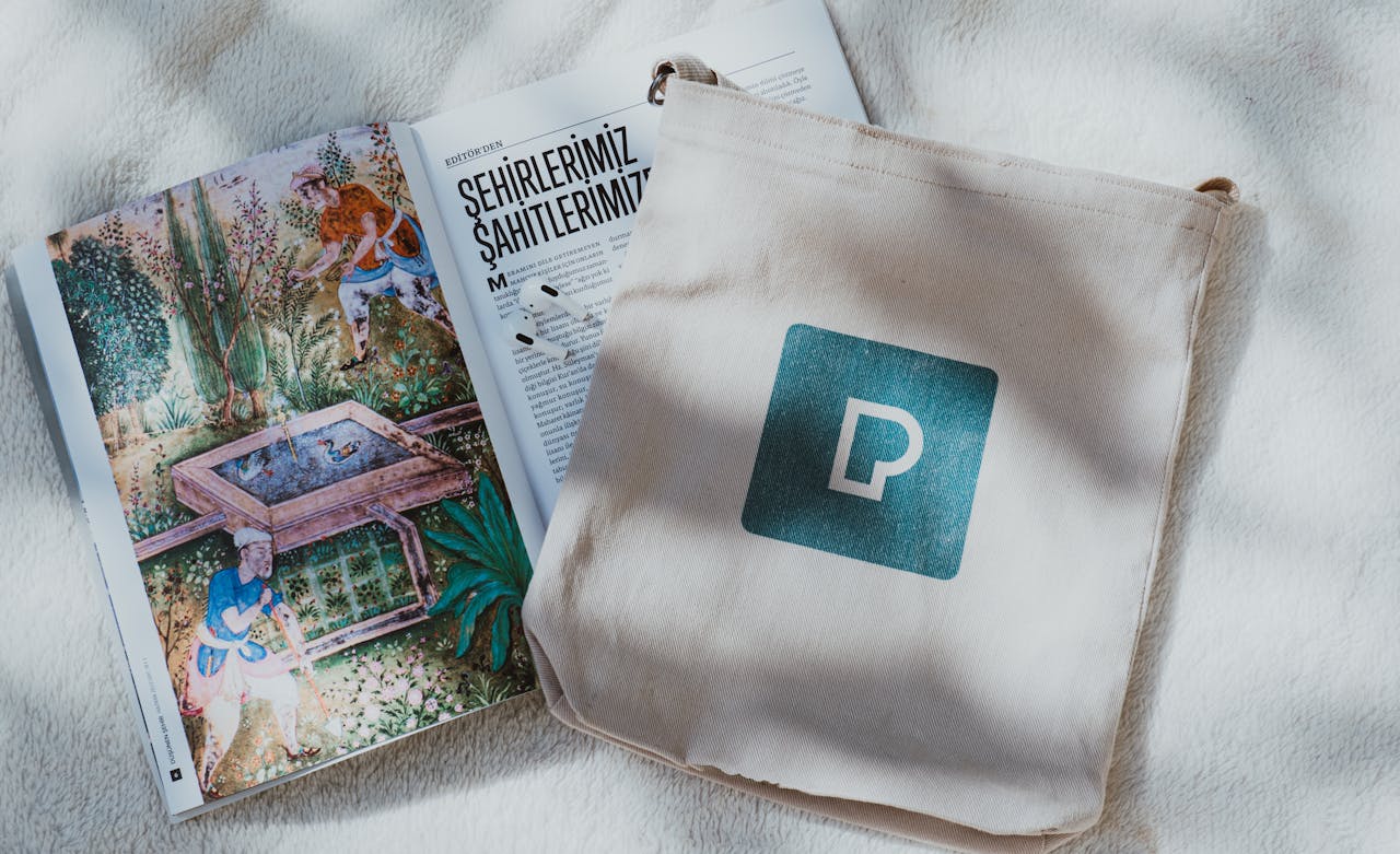A decorative open book and a tote bag with a logo on a soft textured backdrop.